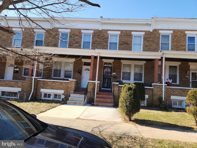 townhome / multi-family property featuring covered porch and brick siding