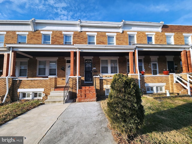 townhome / multi-family property featuring covered porch and brick siding