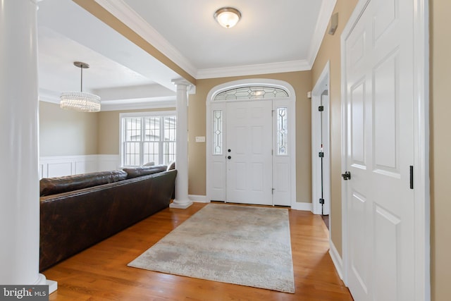 foyer with a wainscoted wall, wood finished floors, decorative columns, and crown molding