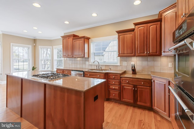 kitchen with light wood finished floors, ornamental molding, light stone countertops, stainless steel appliances, and a sink