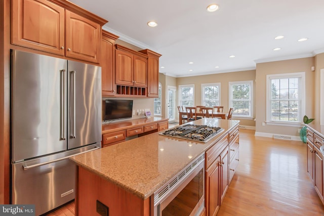 kitchen featuring a center island, crown molding, stainless steel appliances, light wood-style floors, and light stone countertops