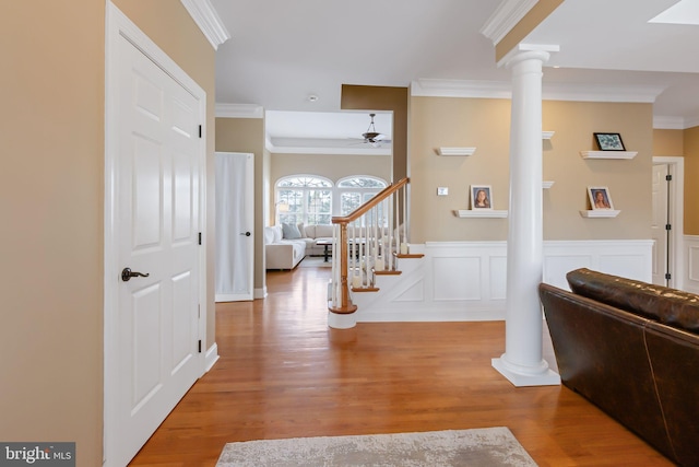 foyer featuring a wainscoted wall, wood finished floors, stairs, ornate columns, and crown molding