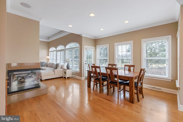 dining room featuring baseboards, crown molding, light wood-style floors, a multi sided fireplace, and recessed lighting