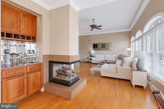 living area featuring ornamental molding, light wood-style flooring, a multi sided fireplace, and a ceiling fan