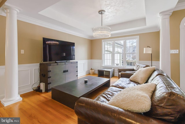 living area with ornate columns, a raised ceiling, and wood finished floors