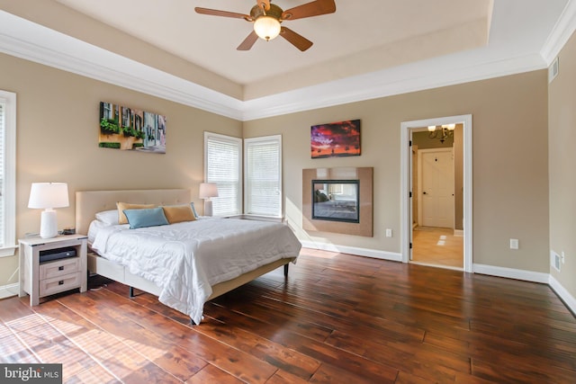 bedroom with hardwood / wood-style flooring, visible vents, a tray ceiling, and baseboards