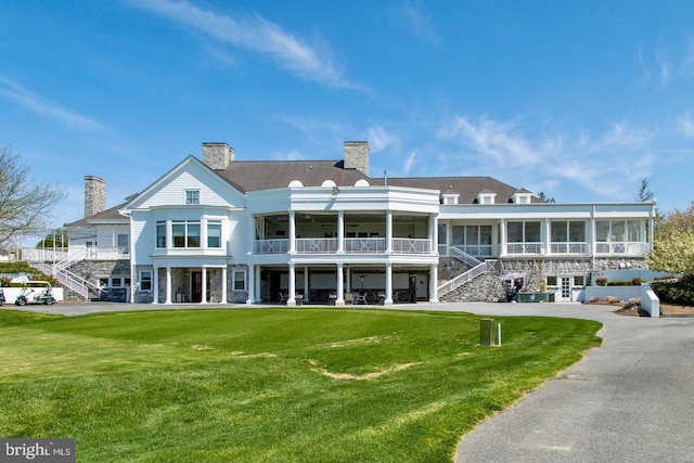 back of house with a sunroom, a chimney, stairway, and a lawn