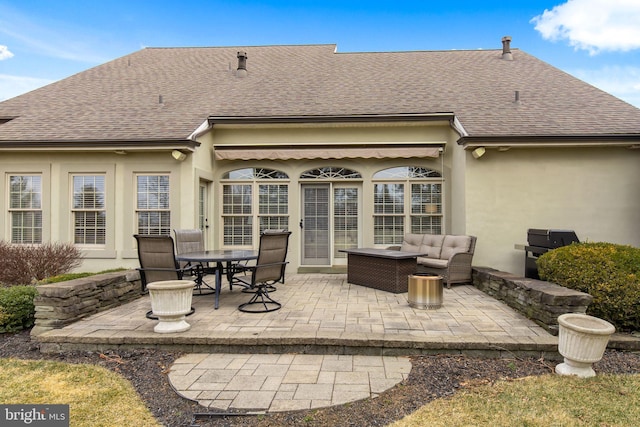 rear view of house with a shingled roof, a patio area, outdoor lounge area, and stucco siding