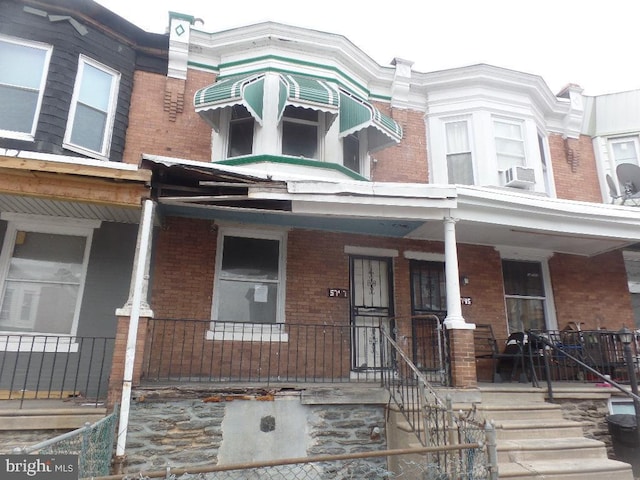 view of property with a porch, cooling unit, and brick siding