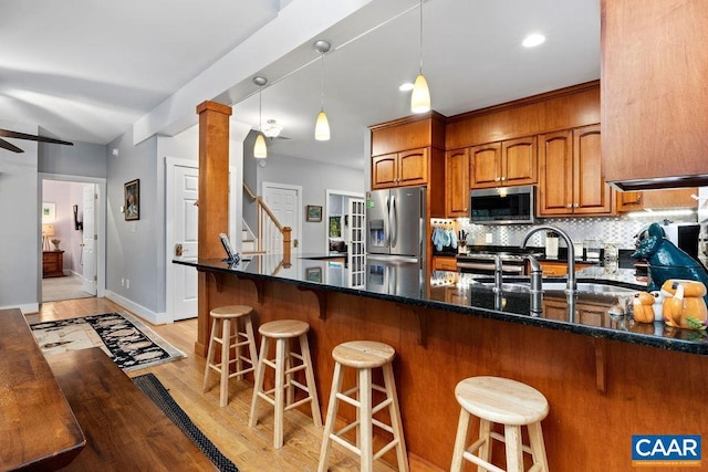 kitchen with light wood-style flooring, appliances with stainless steel finishes, decorative backsplash, brown cabinetry, and dark stone countertops