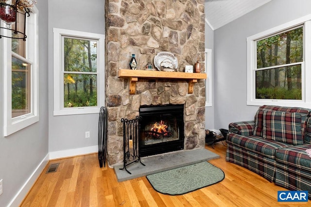 living area with a fireplace, lofted ceiling, visible vents, wood finished floors, and baseboards