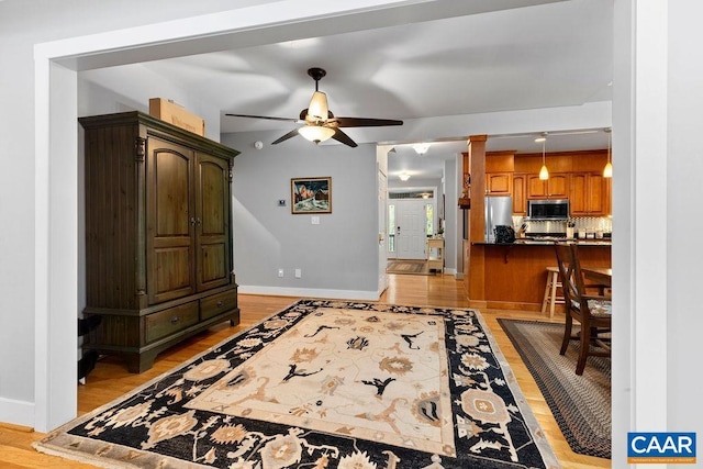 living room with light wood-type flooring, a ceiling fan, and baseboards