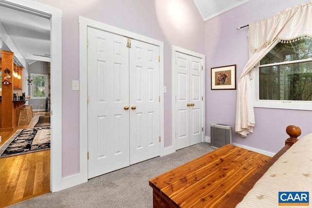 carpeted bedroom featuring vaulted ceiling, baseboards, and two closets