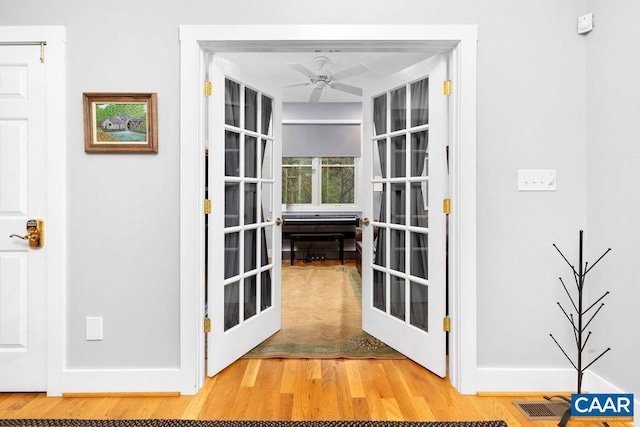 doorway with french doors, light wood finished floors, visible vents, a ceiling fan, and baseboards