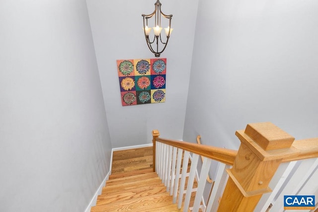 stairway featuring baseboards, wood finished floors, and a notable chandelier