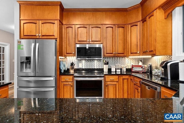 kitchen with stainless steel appliances, dark stone counters, brown cabinetry, and backsplash