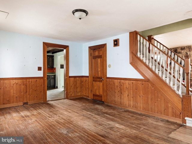 empty room with stairs, wainscoting, hardwood / wood-style flooring, and wooden walls