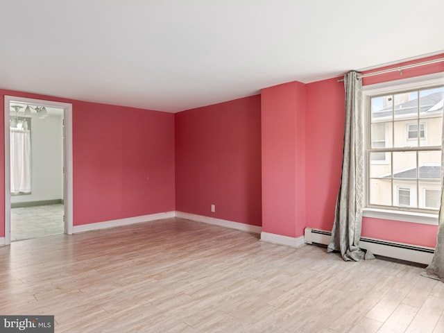 spare room featuring light wood-type flooring, baseboards, and a baseboard heating unit