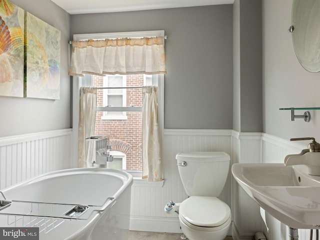 full bath featuring a soaking tub, wainscoting, a sink, and toilet