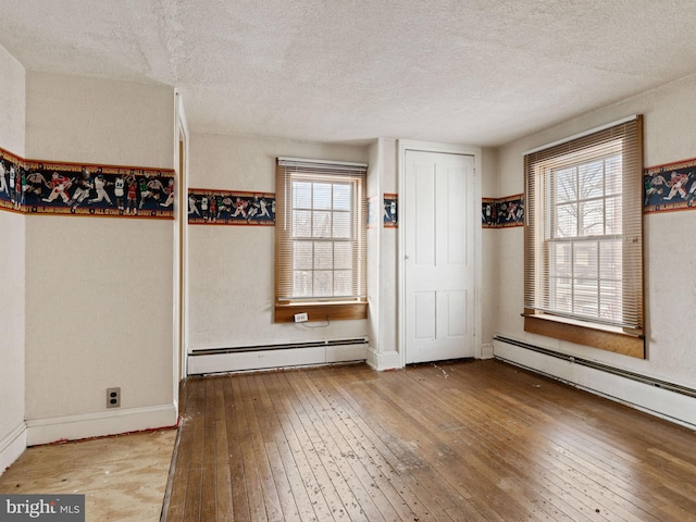 interior space featuring baseboards, a textured ceiling, a baseboard heating unit, and hardwood / wood-style floors