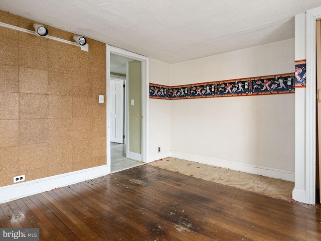 empty room with a textured ceiling, baseboards, and hardwood / wood-style flooring