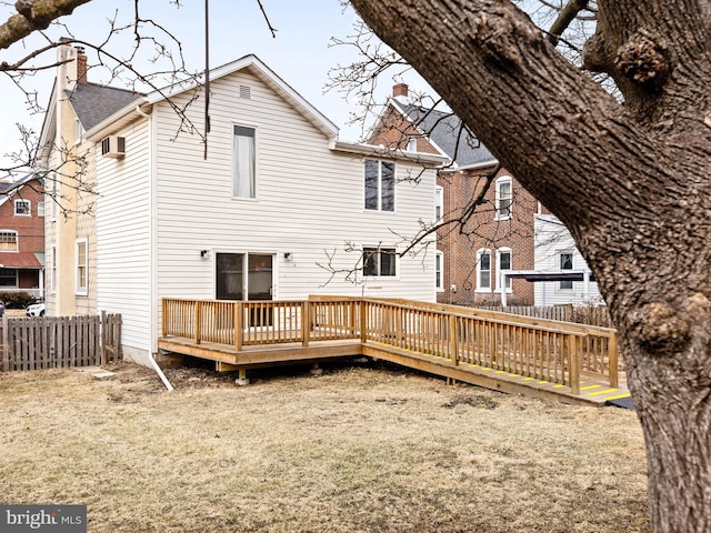 rear view of house featuring a deck, fence, a chimney, and a lawn