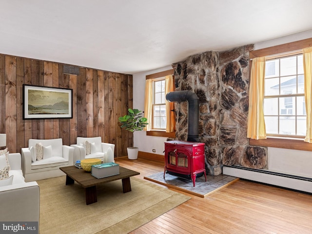 living room featuring a wood stove, baseboard heating, hardwood / wood-style flooring, and wooden walls