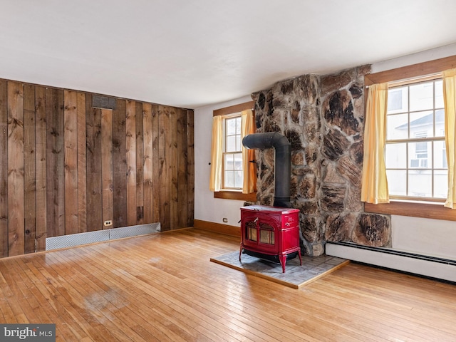 unfurnished living room featuring a wood stove, wooden walls, baseboard heating, and hardwood / wood-style flooring