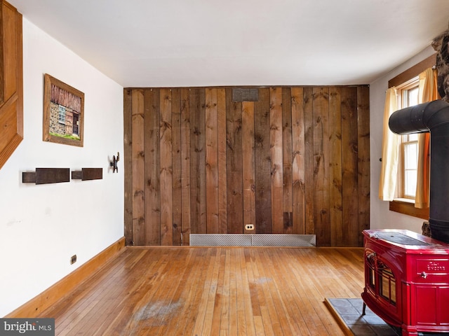 empty room with a wood stove, wood walls, hardwood / wood-style flooring, and baseboards