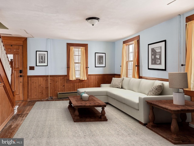 living area with a wainscoted wall, a baseboard heating unit, wood walls, wood finished floors, and stairway