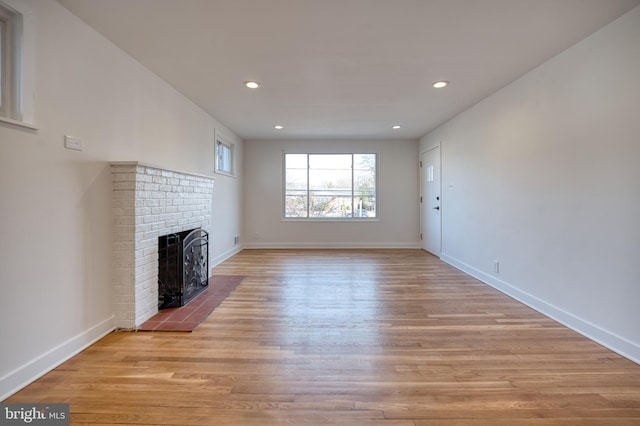 unfurnished living room with light wood-type flooring, a brick fireplace, baseboards, and recessed lighting