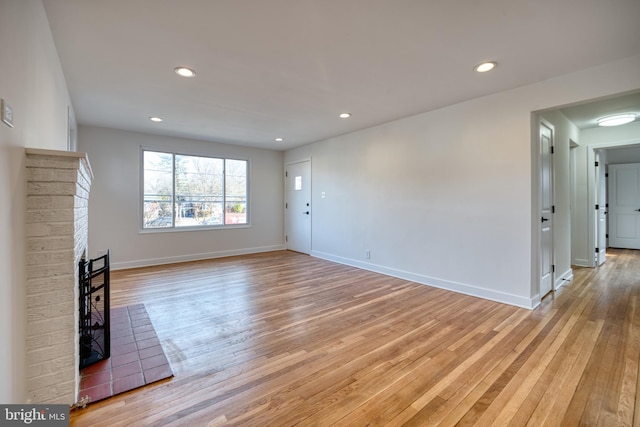 unfurnished living room featuring baseboards, recessed lighting, light wood-type flooring, and a brick fireplace