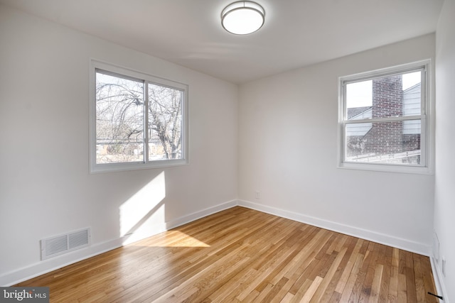 spare room featuring light wood-style floors, plenty of natural light, visible vents, and baseboards