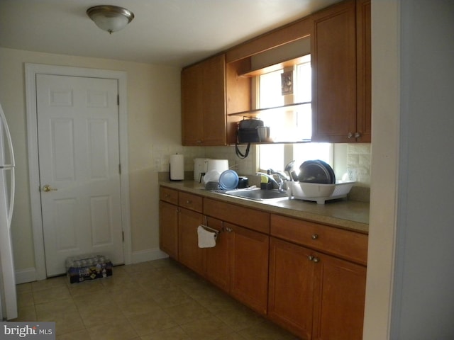 kitchen featuring brown cabinetry, baseboards, open shelves, a sink, and light countertops