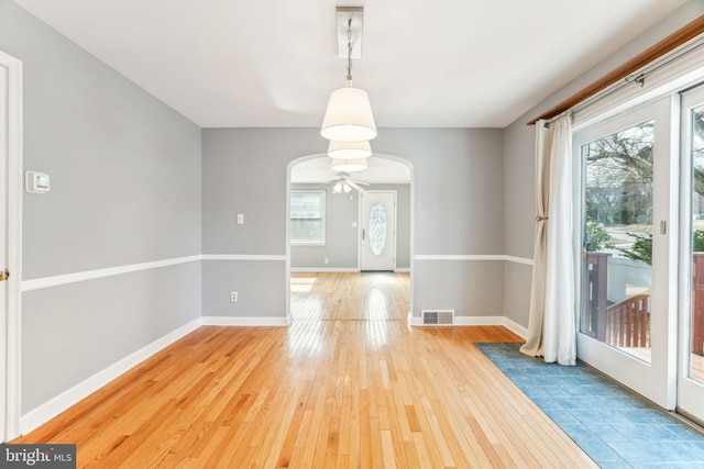 unfurnished dining area featuring light wood-style flooring, visible vents, arched walkways, and baseboards