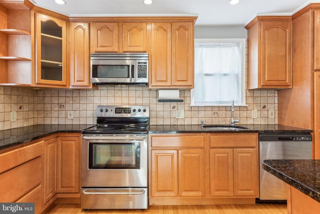 kitchen with stainless steel appliances, tasteful backsplash, glass insert cabinets, a sink, and dark stone countertops