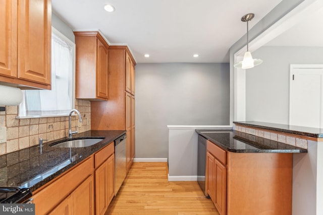 kitchen featuring stainless steel appliances, backsplash, dark stone counters, a sink, and light wood-type flooring