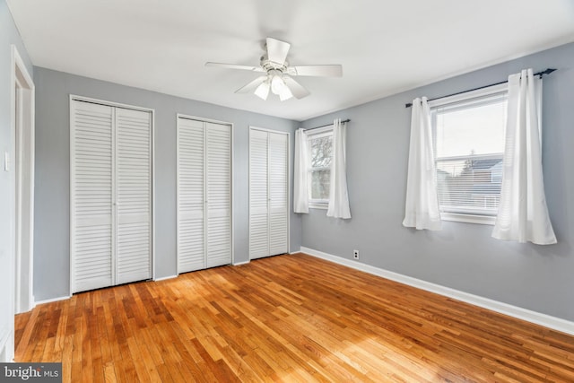 unfurnished bedroom with multiple closets, a ceiling fan, baseboards, and hardwood / wood-style flooring