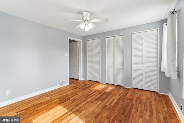 unfurnished bedroom featuring baseboards, wood finished floors, visible vents, and multiple closets