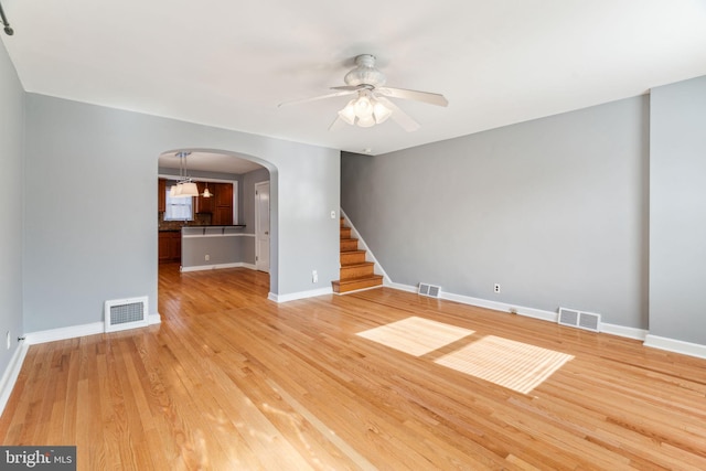 empty room with light wood finished floors, visible vents, and arched walkways