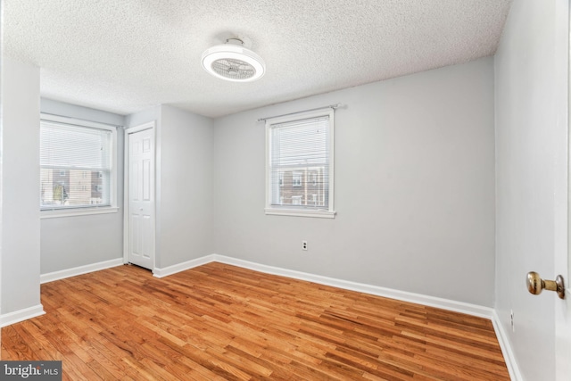 unfurnished room featuring light wood-type flooring, baseboards, and a textured ceiling