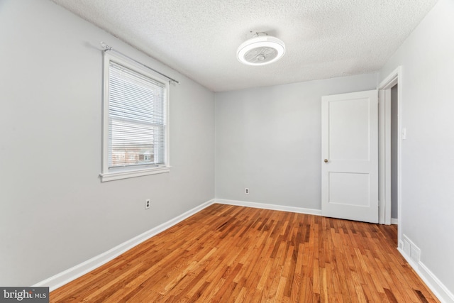 empty room featuring visible vents, light wood-style flooring, baseboards, and a textured ceiling