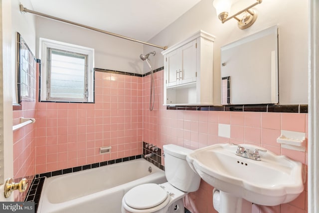 bathroom featuring tile walls, toilet,  shower combination, a sink, and backsplash