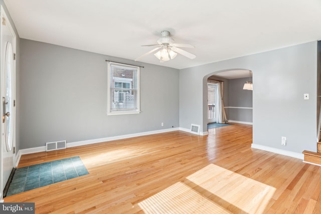 interior space featuring light wood-style flooring, visible vents, arched walkways, and baseboards