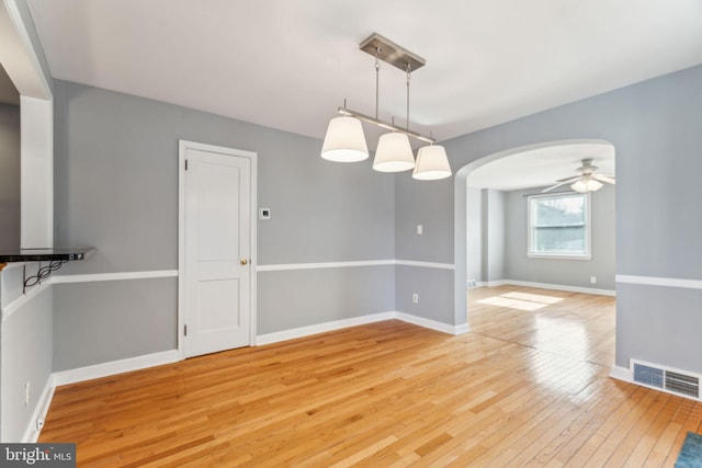 unfurnished dining area with arched walkways, light wood finished floors, visible vents, and baseboards