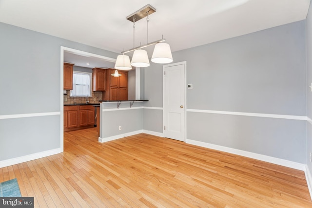 unfurnished dining area featuring baseboards, a sink, and light wood-style floors