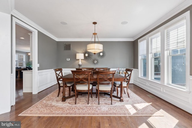 dining area with a wainscoted wall, visible vents, crown molding, and wood finished floors