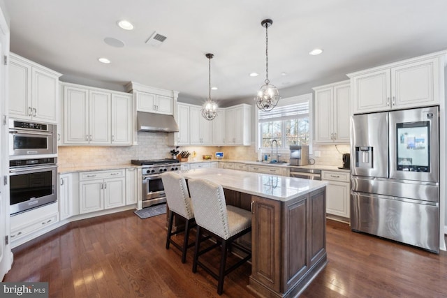 kitchen with dark wood-style flooring, appliances with stainless steel finishes, white cabinetry, a sink, and under cabinet range hood