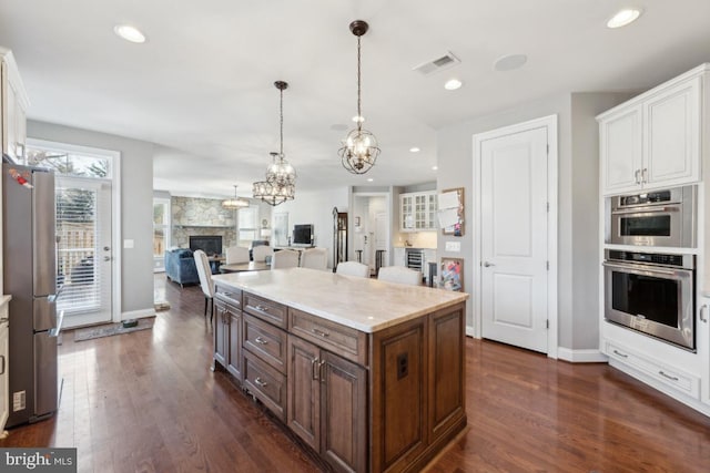 kitchen with visible vents, open floor plan, stainless steel appliances, a fireplace, and white cabinetry