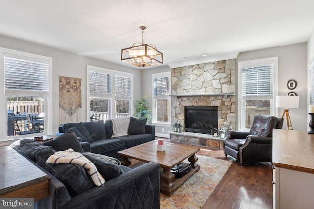 living area with a notable chandelier, dark wood-style flooring, and a stone fireplace